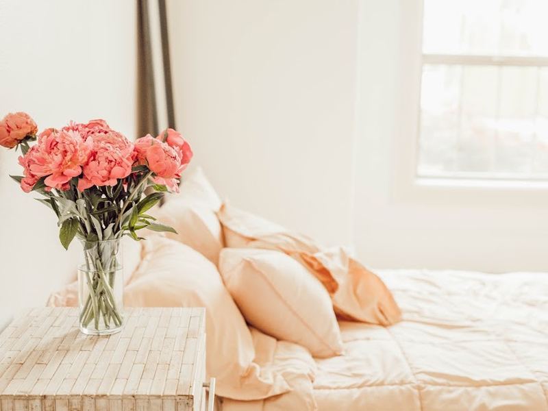 A softly lit bedroom with layered bedding and fresh flowers on a bench.
