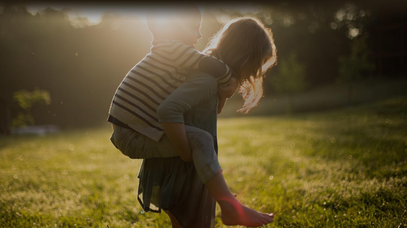 A parent and child playing in an open field of grass at golden hour.